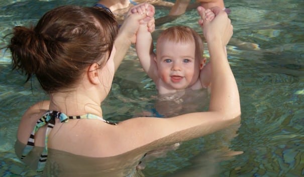 Baby hängandes i tummgreppet i bassängen